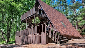 A wooden cabin with a steeply pitched roof, a balcony, and a staircase leading to an upper level. - A-frame Cabin Near Mt. Mitchell | Rustic A-Frame on Private Acre (Burnsville)