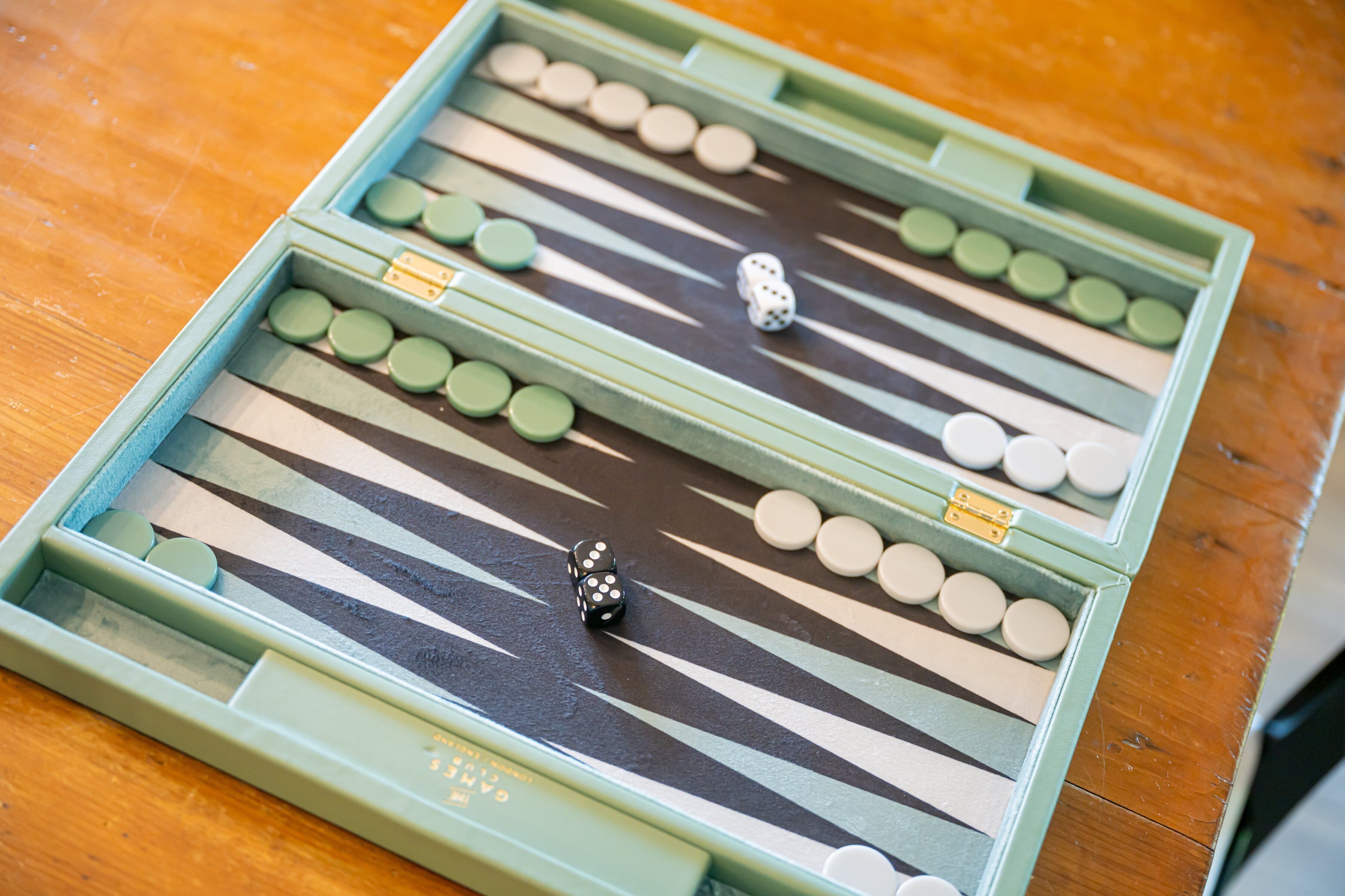 Primer plano de un tablero de backgammon con piezas y dados sobre una superficie de madera.