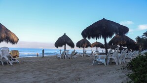 Een strand met rieten parasols en witte ligbedden, gerangschikt langs het zand, met uitzicht op de oceaan.