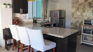 Een moderne keuken met een centraal eiland, barstoelen, een accentmuur van steen en een inbouwoven.