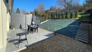 Une terrasse avec une table et des chaises, un barbecue et un espace abrité recouvert d’une bâche verte.