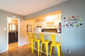 Une cuisine dotée d’un coin bar, de tabourets de bar jaunes et d’un système de crochets de couleurs différentes fixé au mur.