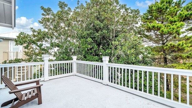 Une terrasse couverte avec une balustrade blanche, une chaise Adirondack en bois et une vue sur des arbres et une maison.