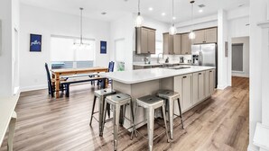 Une cuisine moderne dotée d’un îlot central, de tabourets de bar, de luminaires suspendus et d’un coin repas avec un banc et des chaises.