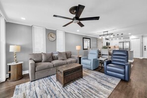 A modern living room with a grey sofa, a blue armchair, a wooden coffee table, and a ceiling fan. - Dolphin Point 106C - Harbor Views & Boat Slip (Destin)