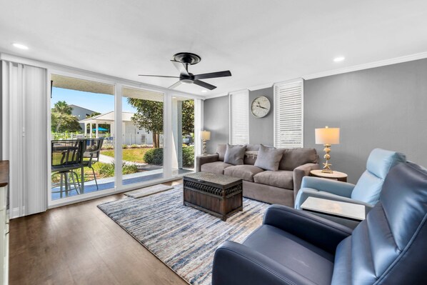 A living room with a ceiling fan, a sofa, a coffee table, and a view through glass doors to an outdoor patio. - Dolphin Point 106C - Harbor Views & Boat Slip (Destin)