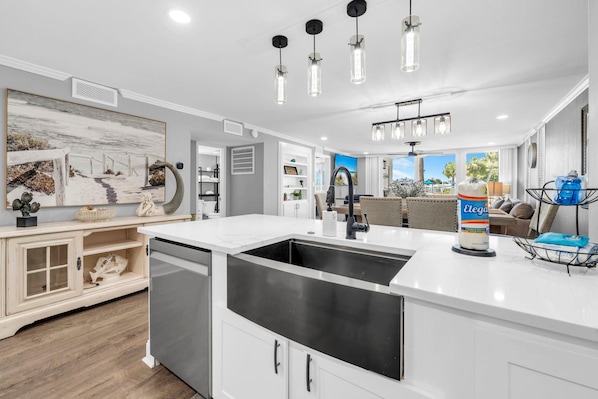 A modern kitchen with a large island, stainless steel appliances, pendant lighting, and a view to the outdoor area.