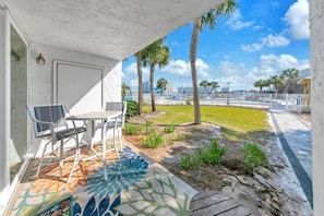 A covered outdoor area with a table and chairs, a patterned rug, and a view of a pool and palm trees. - Dolphin Point 106C - Harbor Views & Boat Slip (Destin)