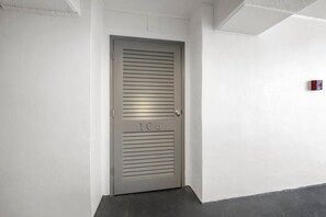 A metallic door with horizontal slats, marked with the number 106, in a hallway with white walls and a fire alarm on the right.