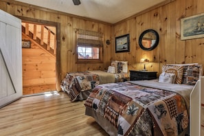 A wooden cabin bedroom with two beds, a window, a mirror, and a staircase leading to an upper level. - NEW LISTING !!! RUSTIC MEADOW AT LADYBUG LAKE (Morganton)