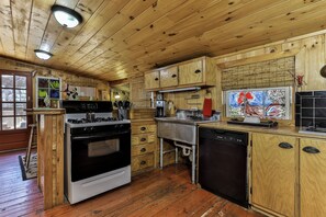 Ein Holzblockhaus-Innenraum mit einer Küche, die einen Herd, ein Backofen, eine Spüle und einen Kühlschrank umfasst.