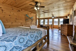 A wooden cabin interior with a bed, a television, and a ceiling fan.