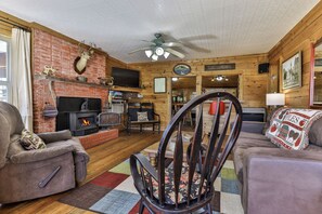 Ein gemütliches Wohnzimmer mit Kamin, Holzwänden, einem Fernseher und einem Deckenventilator.