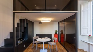A modern interior with a dining area featuring a round table and four chairs, a staircase with dark railings, and a bright pendant light.