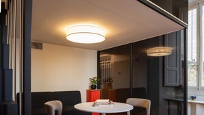A modern room with a round table and four chairs, a sofa, and a red side table with a plant.
