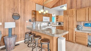 A kitchen with wooden cabinets, a central island with stools, a microwave, and a gas stove. - the Zephyr Shore in Roads End (Lincoln City)