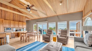 A spacious living area with a wooden ceiling, a ceiling fan, and a view of the outdoors through large windows. - the Zephyr Shore in Roads End (Lincoln City)