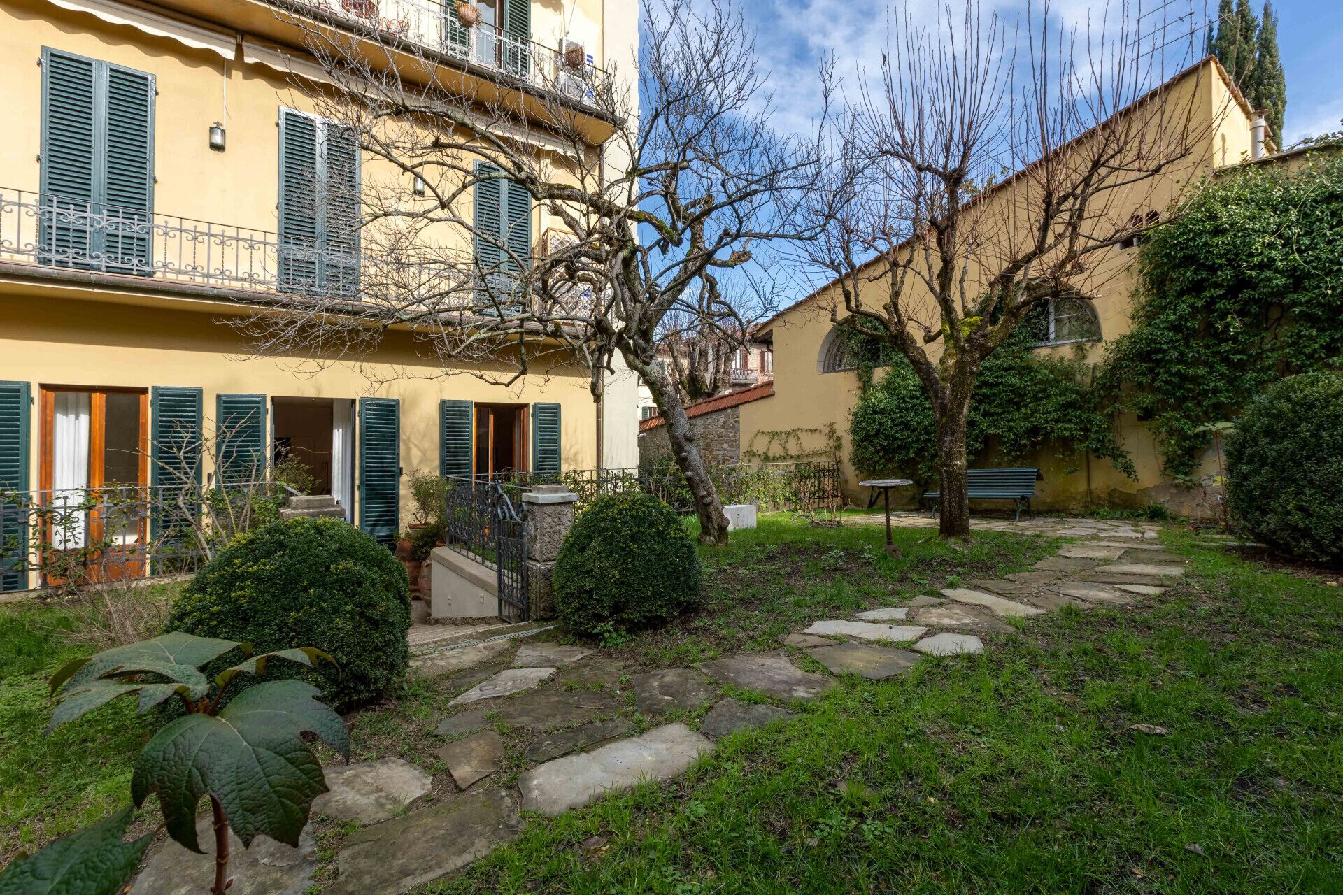 A courtyard with stone pathways, a small garden, and a building with green shutters and balconies.