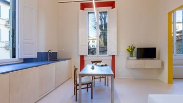 A compact kitchen with a dining area, a TV mounted on the wall, and a window with a view of buildings outside.