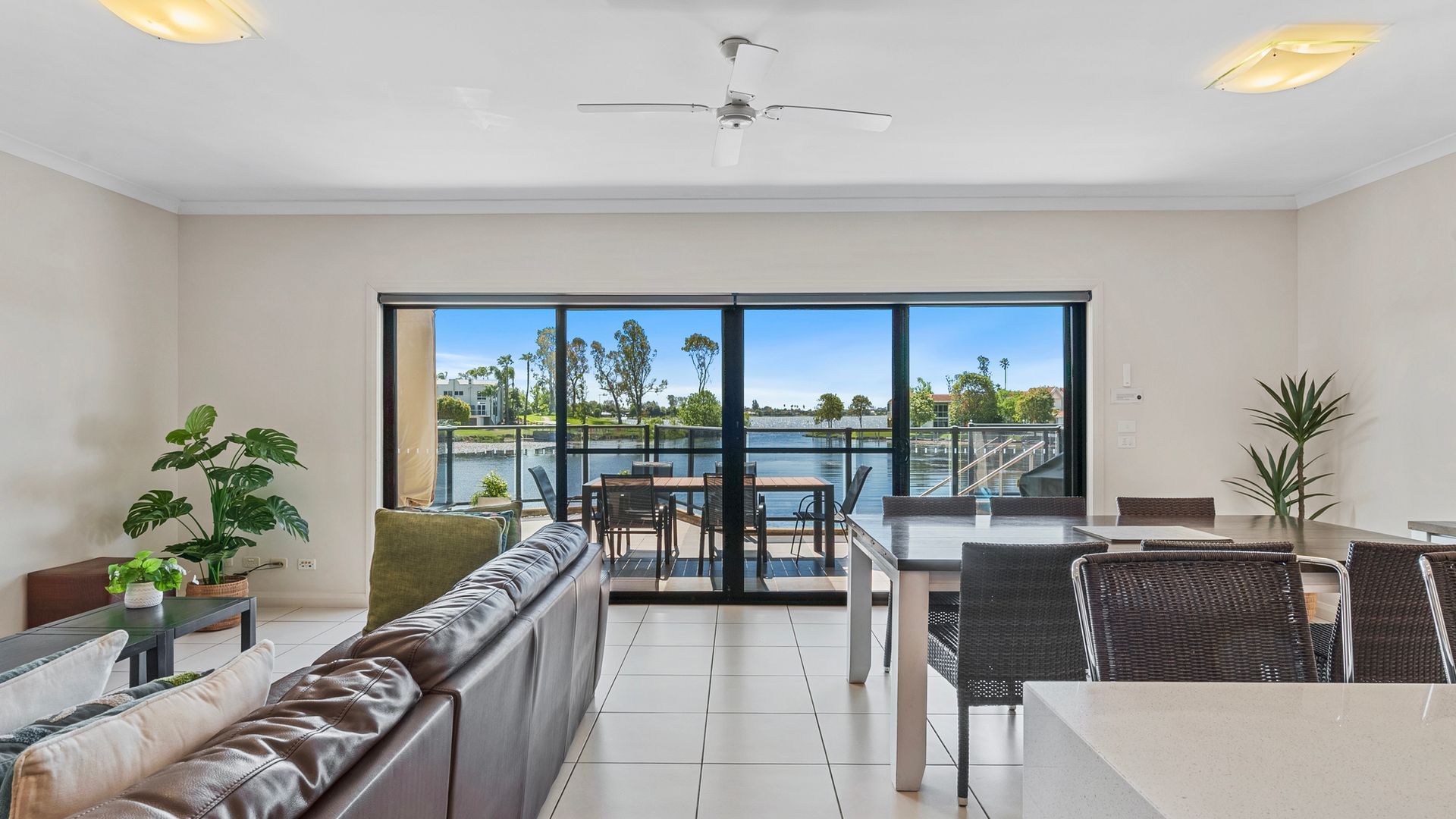 A modern living room with a large window, a ceiling fan, and a dining area with outdoor seating.
