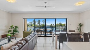 A modern living room with a large window, a ceiling fan, and a dining area with outdoor seating.