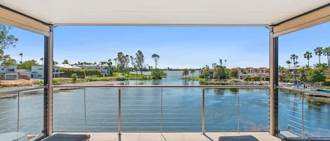 A balcony with a view of a river, lounge chairs, and a clear sky.