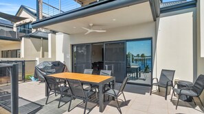 Un patio exterior con mesa y sillas, un espacio de estar cubierto y vista a un cuerpo de agua.