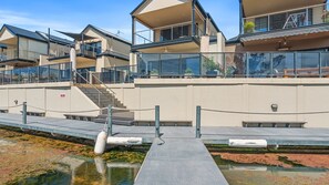 A modern building with multiple balconies, a staircase, and a dock extending into a body of water.
