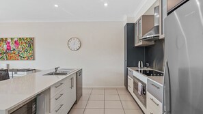 A modern kitchen with a stainless steel refrigerator, a microwave, and a stove. There is a sink with a faucet, and a clock on the wall.