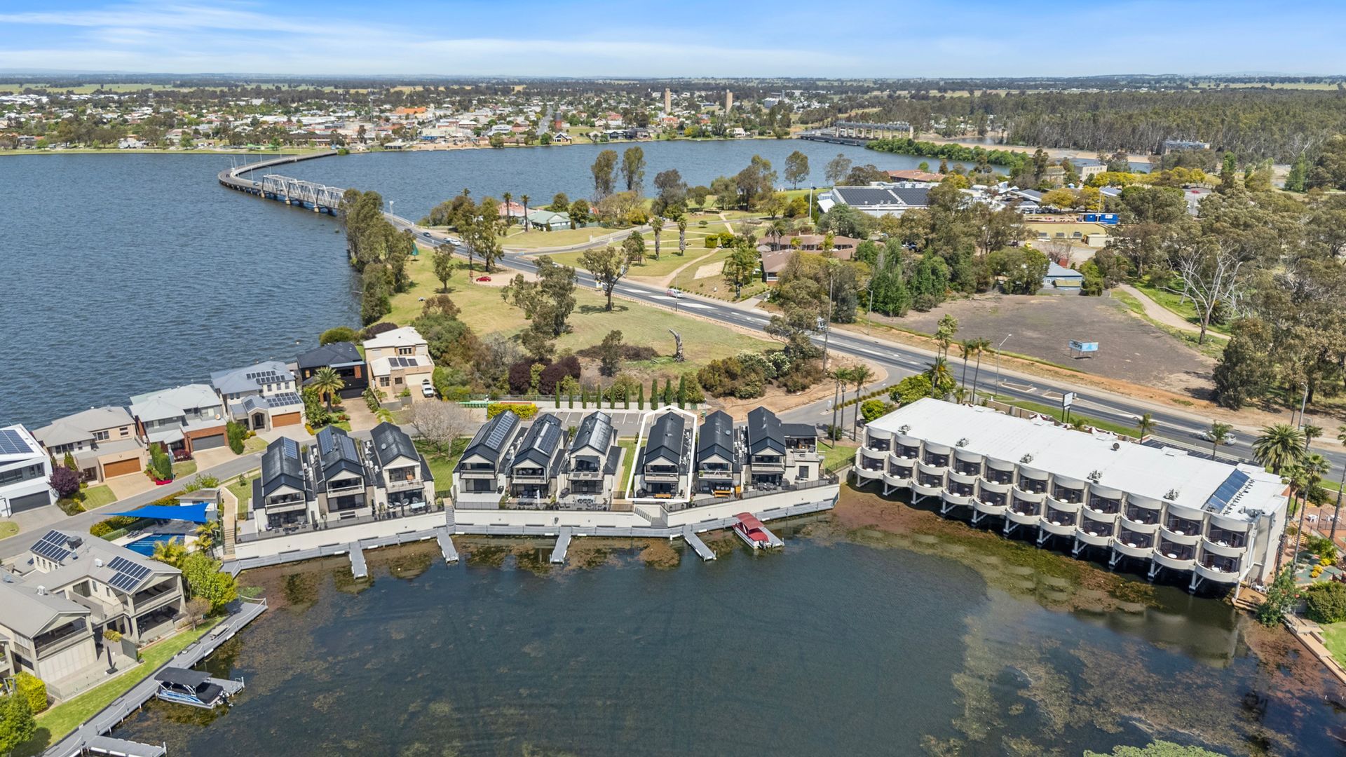 An aerial view of a lakeside residential area with modern houses, a bridge, and a marina.