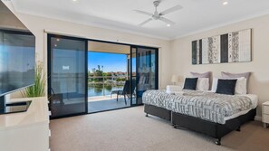Un dormitorio moderno con cama, mesita de noche, ventilador de techo y vistas a una piscina y edificios.