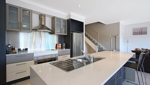 Una cocina moderna con electrodomésticos de acero inoxidable, una isla central con lavamanos y una escalera que sube a otro nivel.