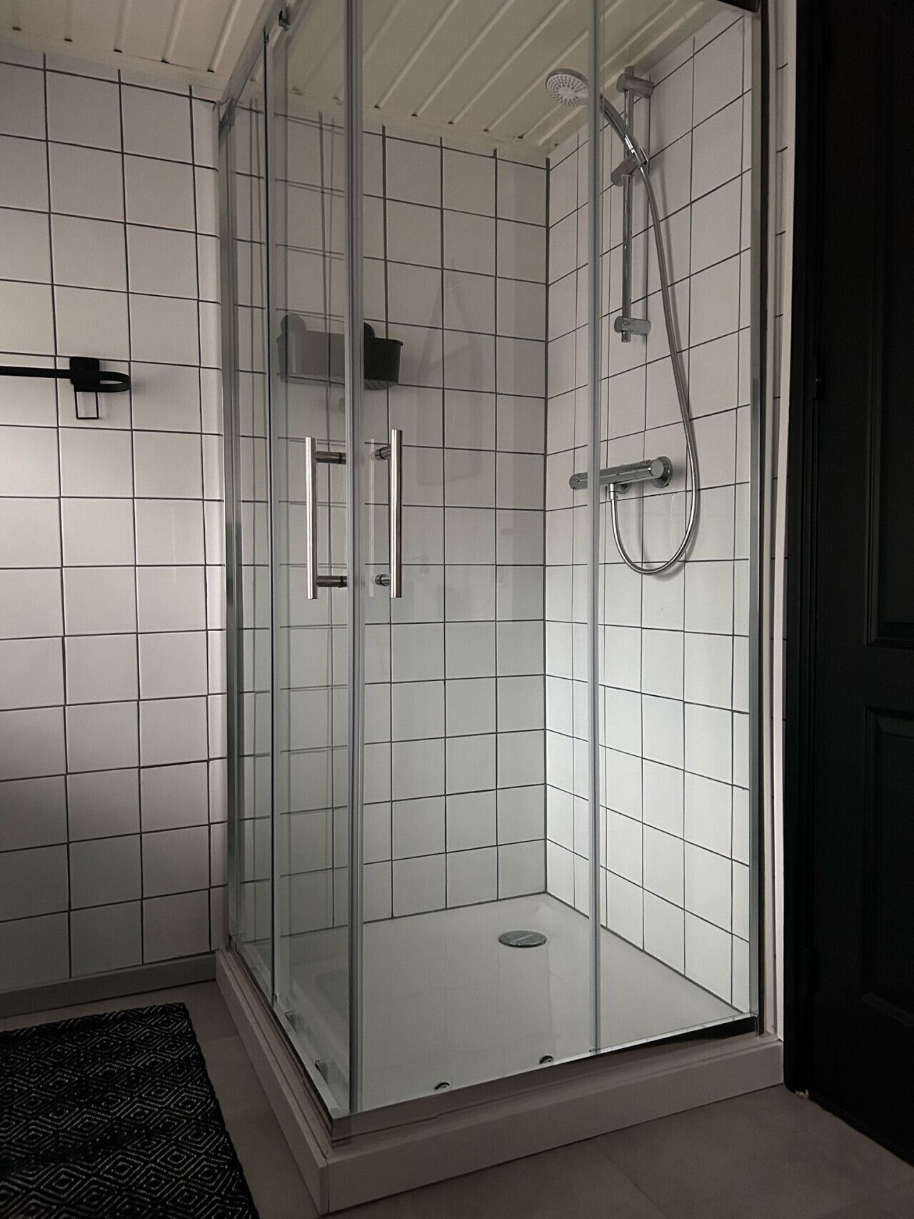 A glass-enclosed shower with a tiled floor and a black mat.