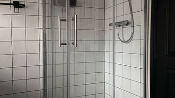 A glass-enclosed shower with a tiled floor and a black mat.