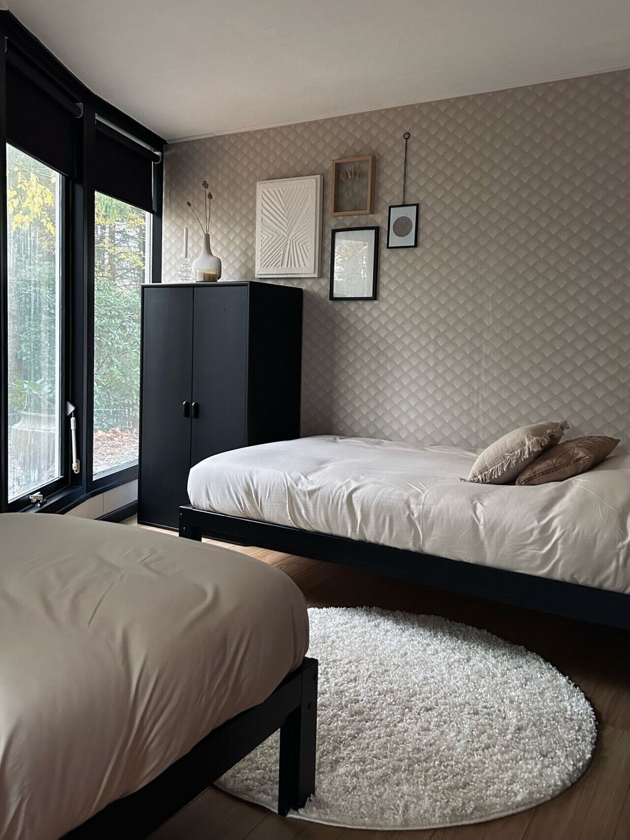 A bedroom with two beds, a wardrobe, and a window with a view of trees.