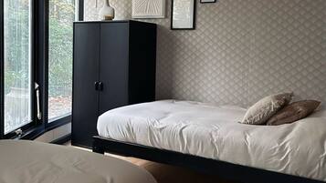 A bedroom with two beds, a wardrobe, and a window with a view of trees.