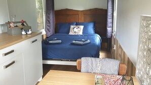 Quarto compacto com cama, mesa de cabeceira e pequena área de trabalho.
