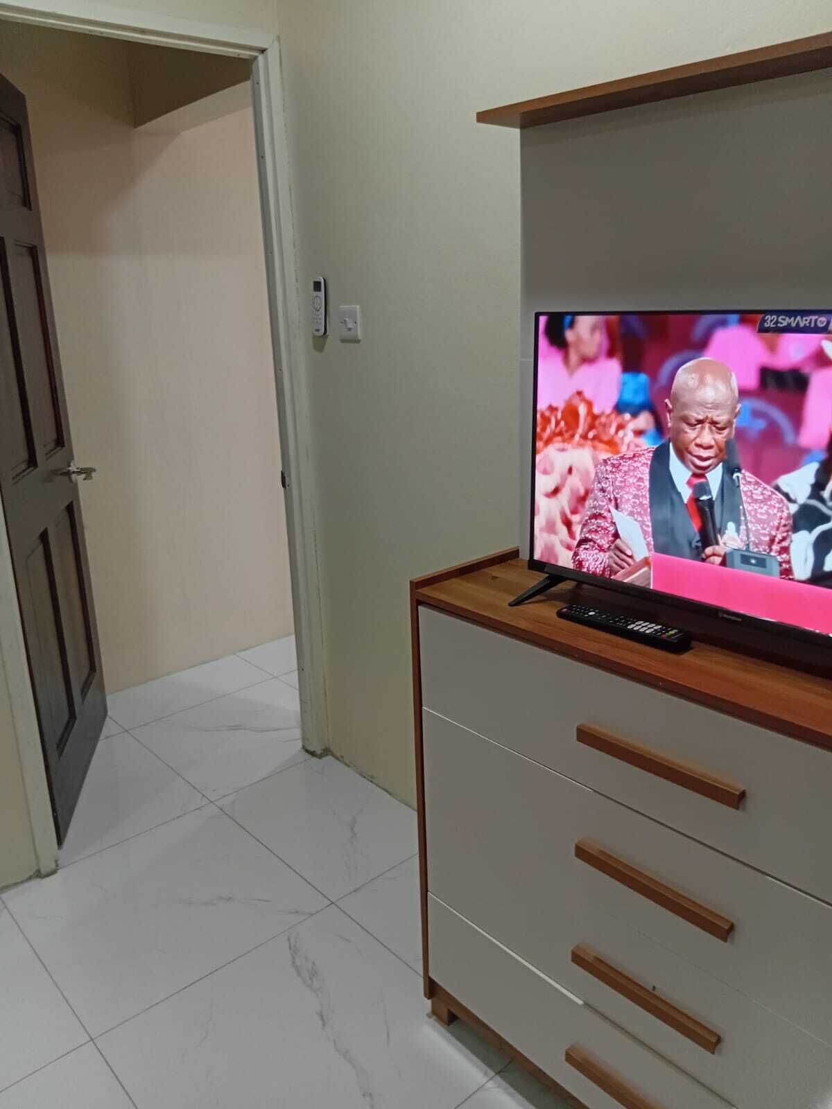 A television on a wooden cabinet with a remote control, a door, and a light switch on the wall.
