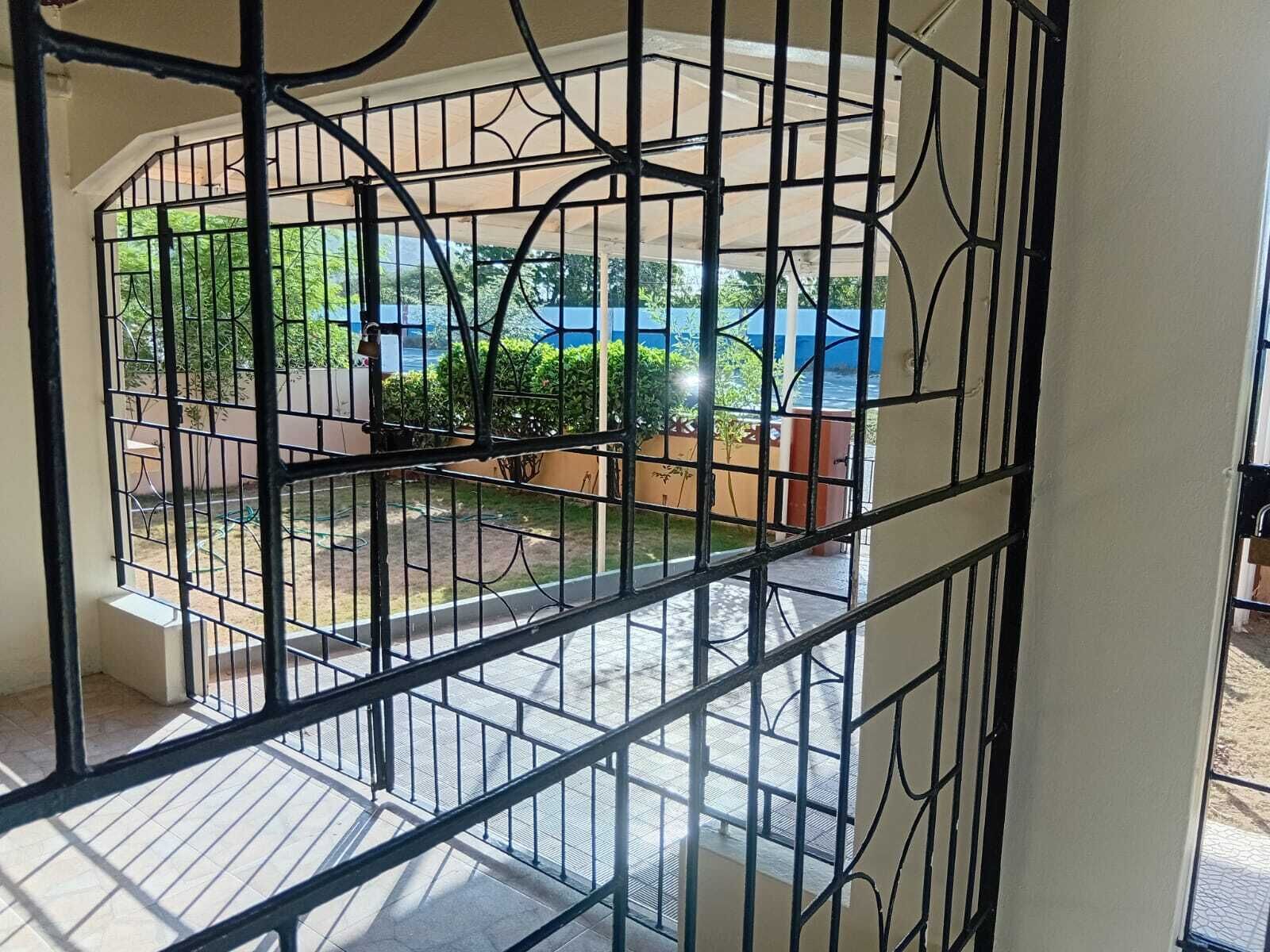 A view through a barred window with a balcony, outdoor furniture, and a blue car in the background.