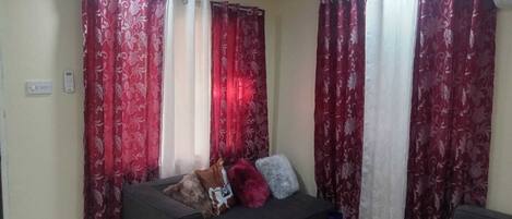 A living room with a sofa, a glass coffee table, and red patterned curtains.