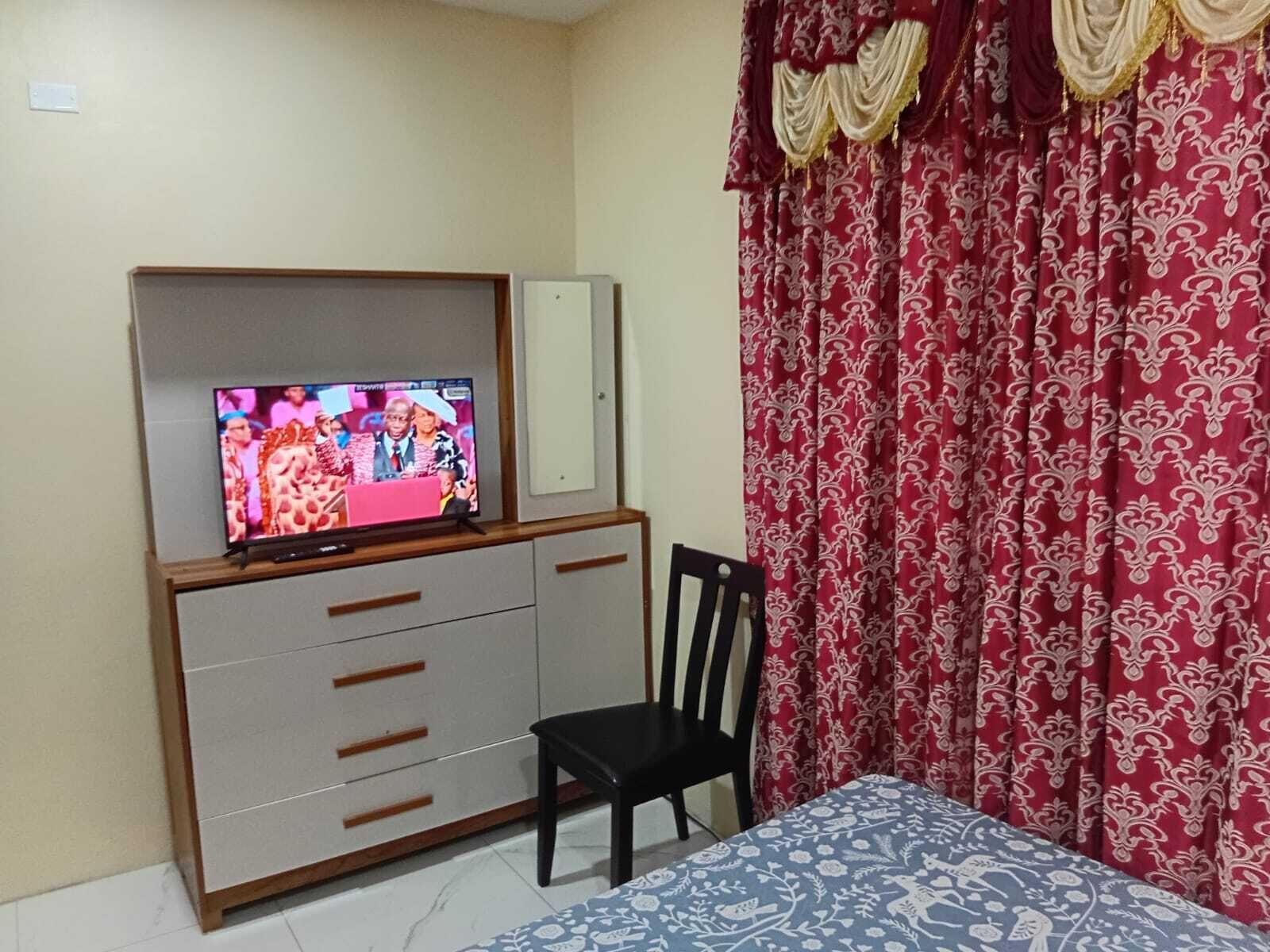 Un dormitorio con cama, televisor sobre un mueble bajo, una silla y un armario.