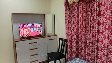 A bedroom with a bed, a TV on a stand, a chair, and a wardrobe.