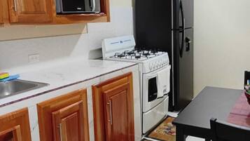 Una cocina con armarios de madera, microondas, cocina a gas, refrigerador y una mesa de comedor con sillas.