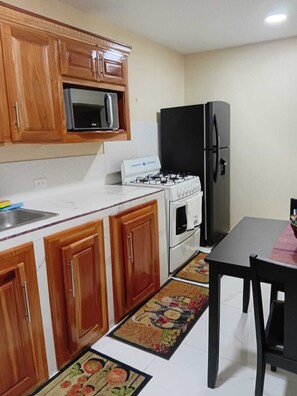 A kitchen with wooden cabinets, a microwave, a gas stove, a refrigerator, and a dining table with chairs. - Charming 2-bedroom house in Portmore with WiFi, AC (Portmore)