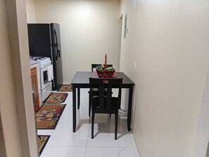 A narrow kitchen with a dining table and chairs, a refrigerator, and a gas stove. - Charming 2-bedroom house in Portmore with WiFi, AC (Portmore)