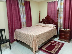 A bedroom with a bed, a wooden headboard, a nightstand, a chair, and a patterned rug. - Charming 2-bedroom house in Portmore with WiFi, AC (Portmore)