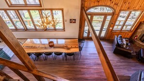 A spacious loft-style room with a large dining table, wooden floors, and multiple windows offering views of the outdoors. - Spacious Chalet Near Stratton and Mt. Snow w/Indoor Hot Tub, Fireplace, Firepit (Wardsboro)