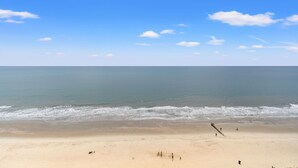 Een strand met een heldere lucht, rustige zee en enkele wandelaars.
