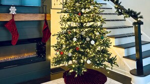 Un árbol de Navidad con luces y adornos en una sala de estar moderna con una escalera.