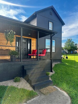 Et moderne hus med en veranda, to røde stole og en lille trappe op til indgangen.